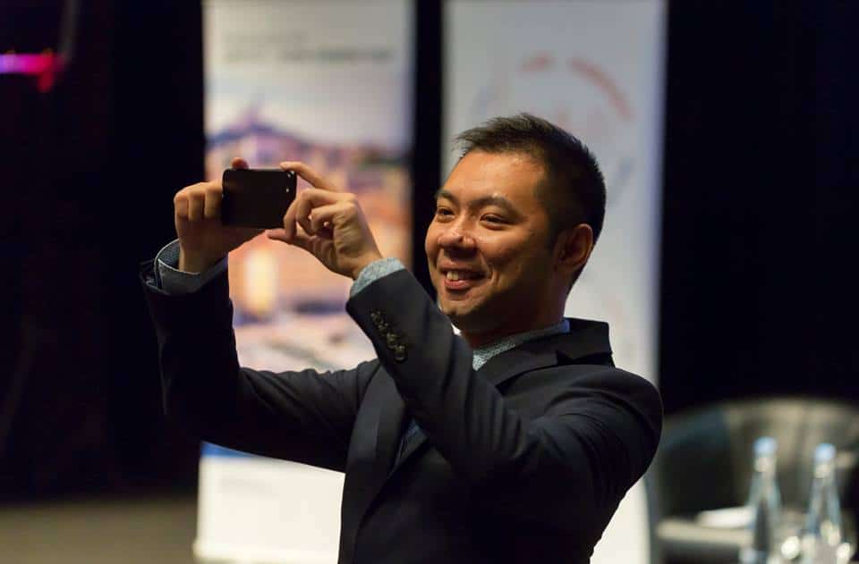 A speaker at the World Bridge Tourism taking a picture of the audience